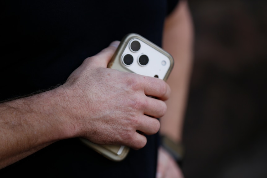 A man in a black shirt holds an iPhone in his hand.