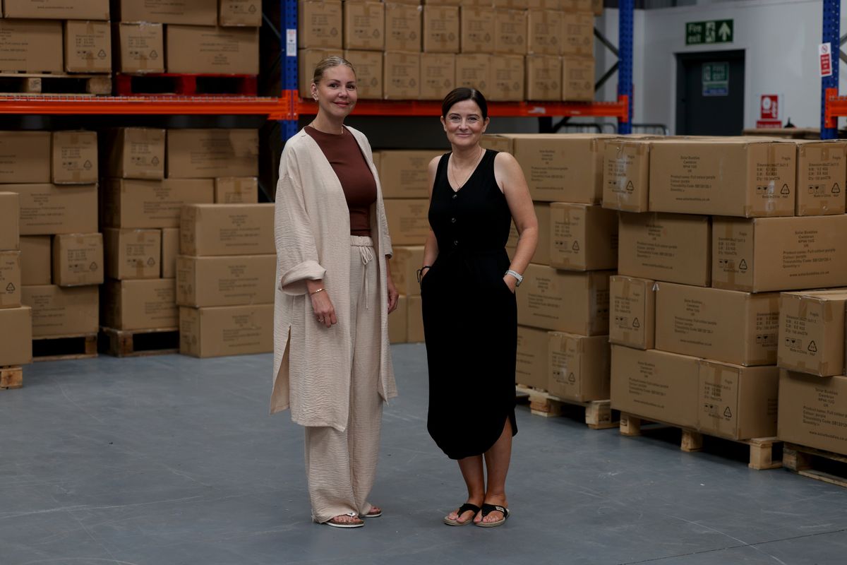 Two smiling women stood by boxes in a warehouse