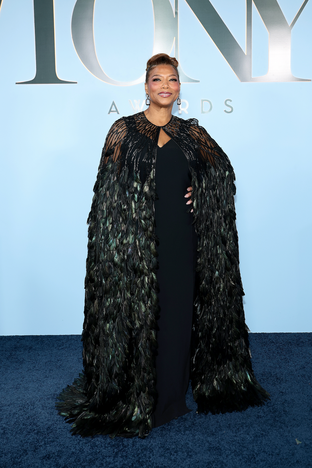 Person in black feathered cape on blue carpet at event.