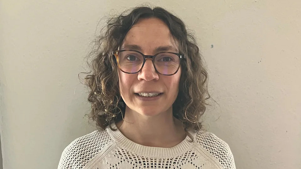 a woman with brown curly hair and glasses, wearing a white top