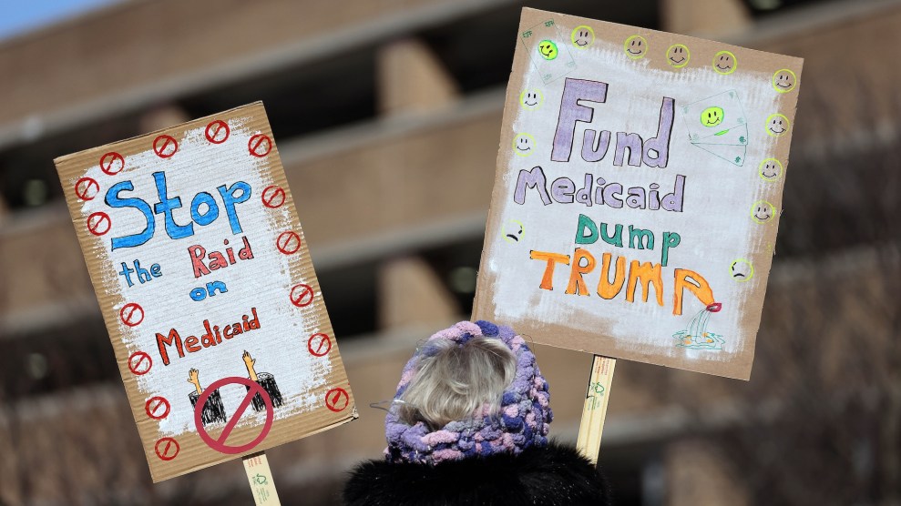 A person holding up signs that say "Stop the raid o Medicaid" and "Fund Medicaid Dump Trump"