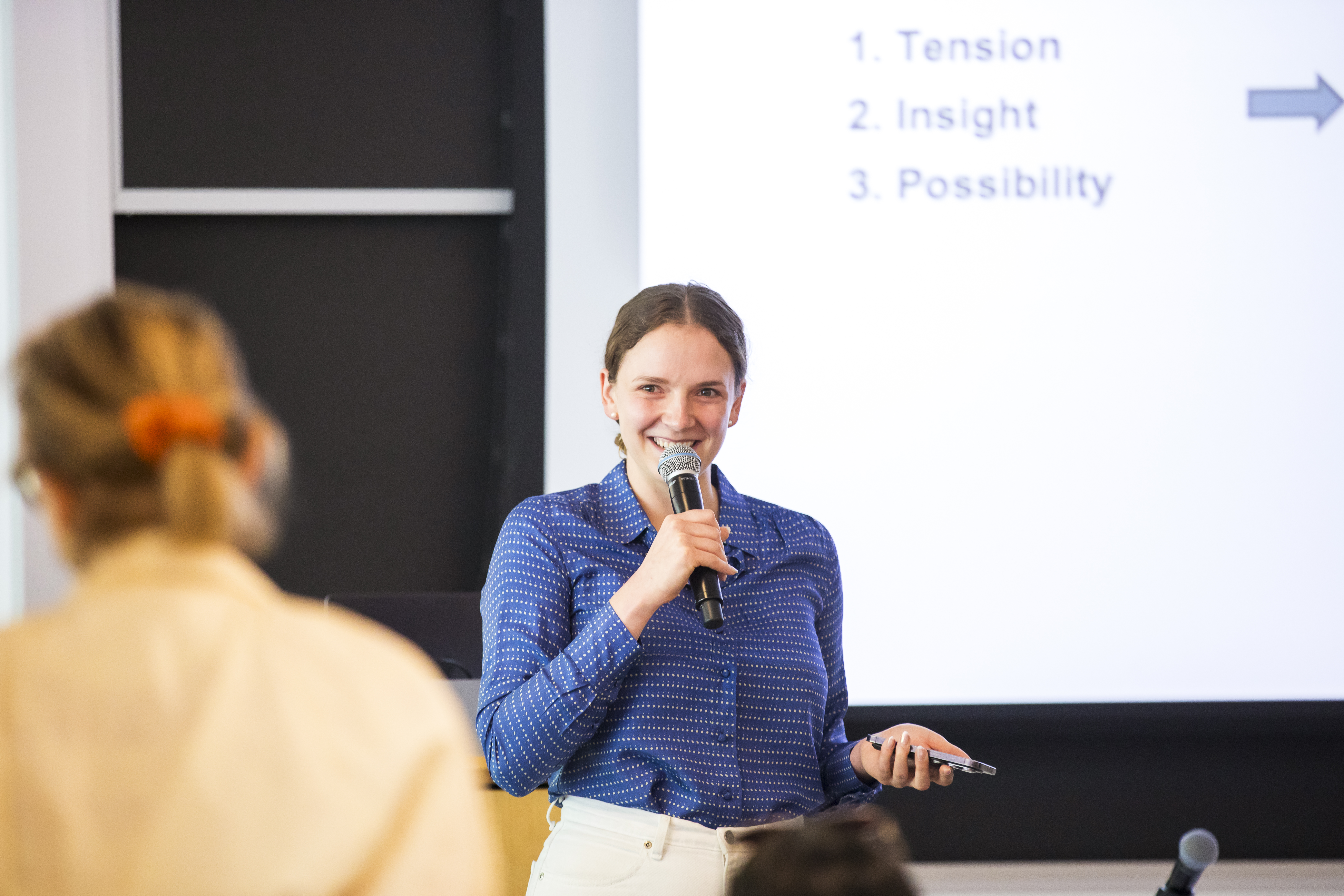 Student with a microphone presenting in front of a calss.