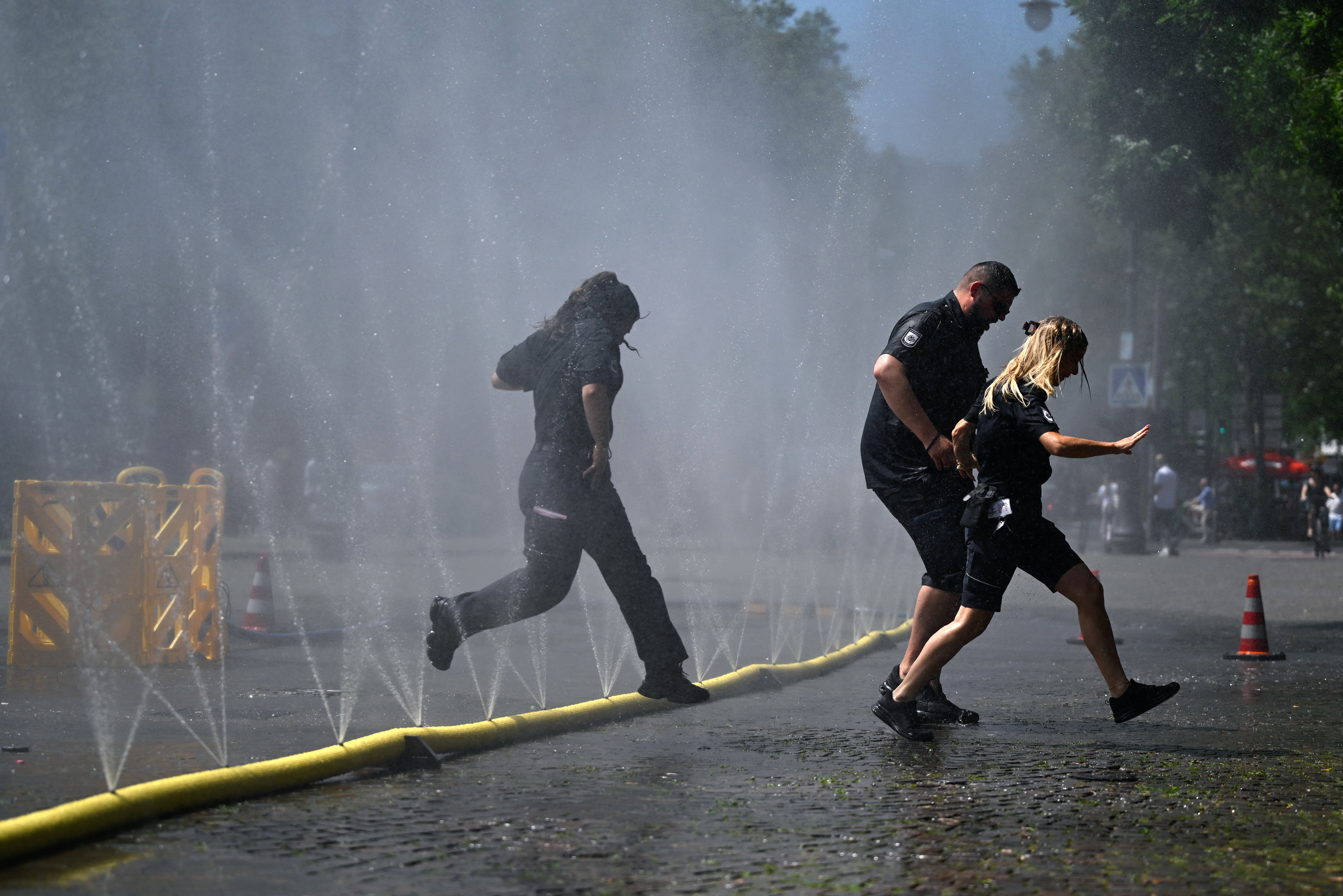 Employees of the public order office run over water hoses spilling water to provide relief from the summer heat as part of Cologne's climate adaptation measures