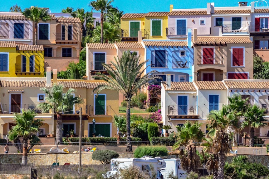 On a bright sunny day, multi-coloured terrace homes cascade down a hill to a beach.