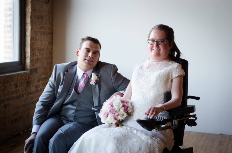 Greg, left, and Rebecca Anger are seated in wheelchairs while Greg is in a gray wedding tuxedo and Rebecca wears a white wedding dress and holds a bouquet of flowers