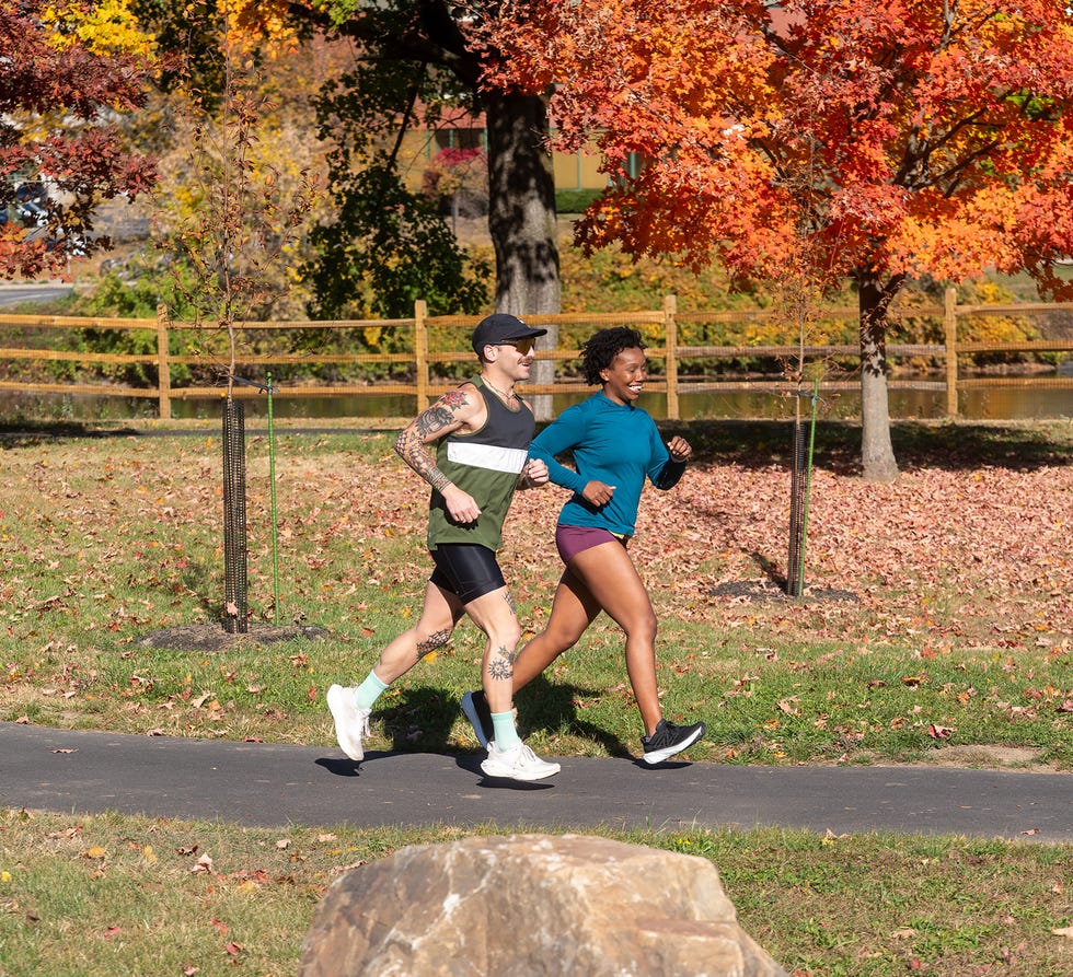 Two joggers running on a path surrounded by autumn foliage.