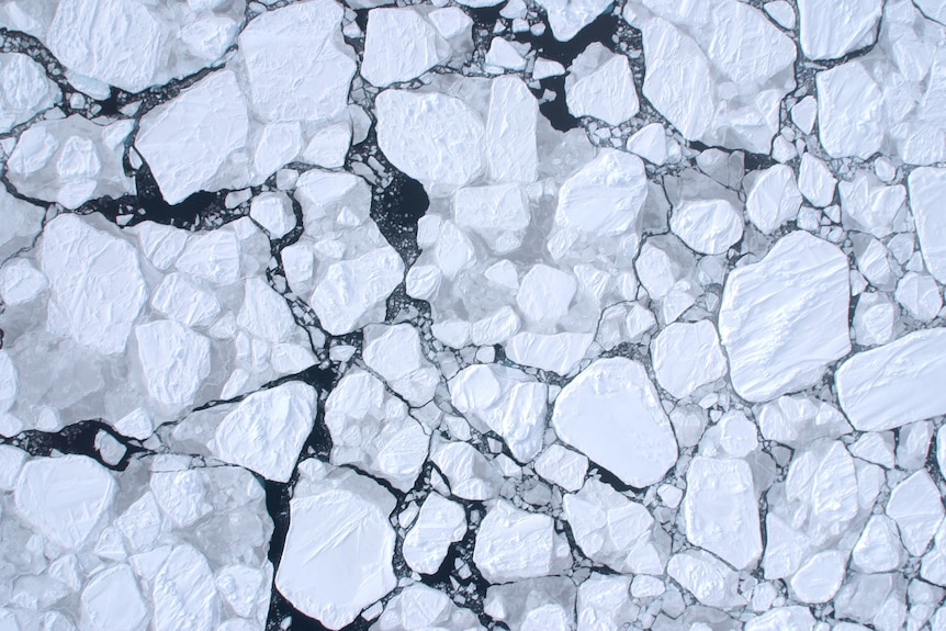 An aerial view of white ice breaking up on a black sea