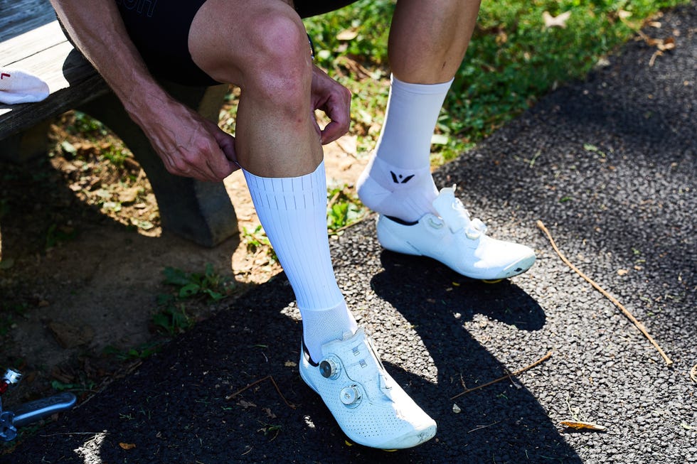 Person adjusting knee-high white cycling socks with white cycling shoes. Person adjusting knee-high white cycling socks with white cycling shoes.