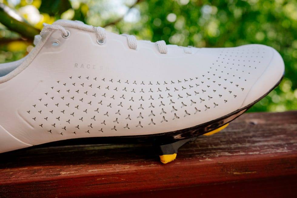 Close-up of a white cycling shoe with perforations and a yellow cleat. Close-up of a white cycling shoe with perforations and a yellow cleat.