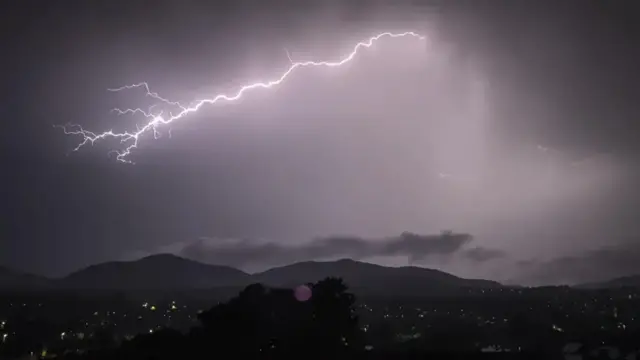 A long strand of lighting stetches over Edinburgh. It can be seen splintering into different strands to the left of the picture