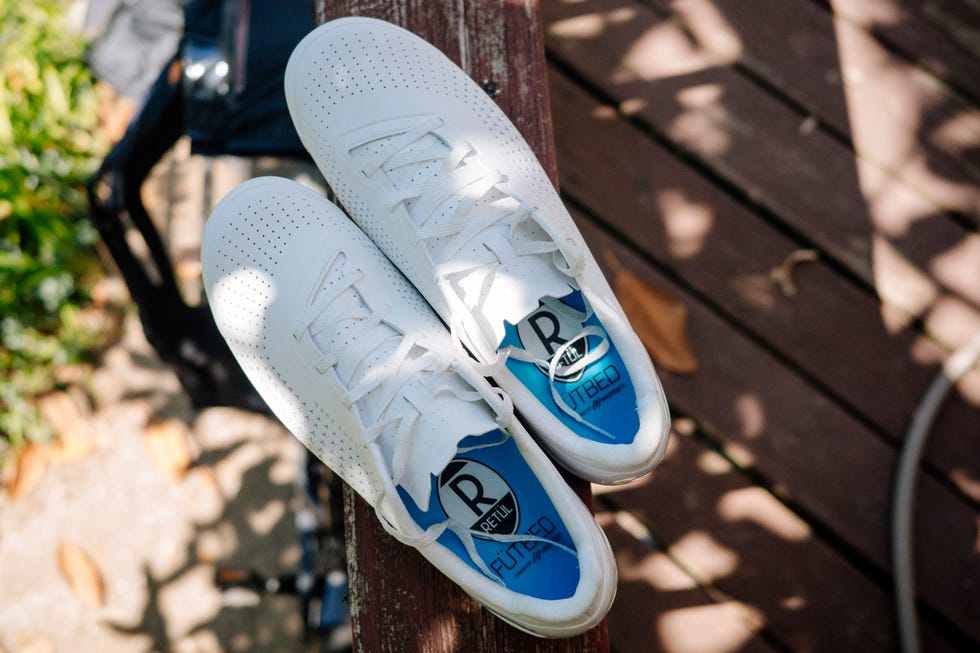 Pair of white cycling shoes with blue insoles on wooden surface. Pair of white cycling shoes with blue insoles on wooden surface.