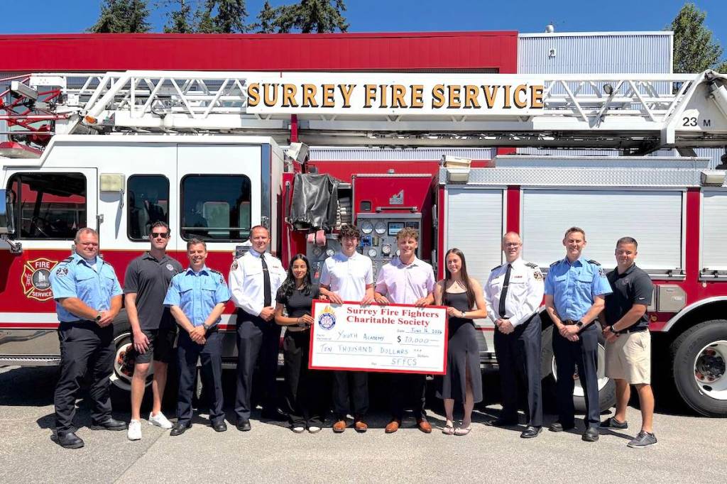 Four Surrey students and firefighters with a prop cheque for $10,000 in scholarships following the 2026 Surrey Fire Fighters Youth Academy. (Contributed to Surrey Now-Leader)