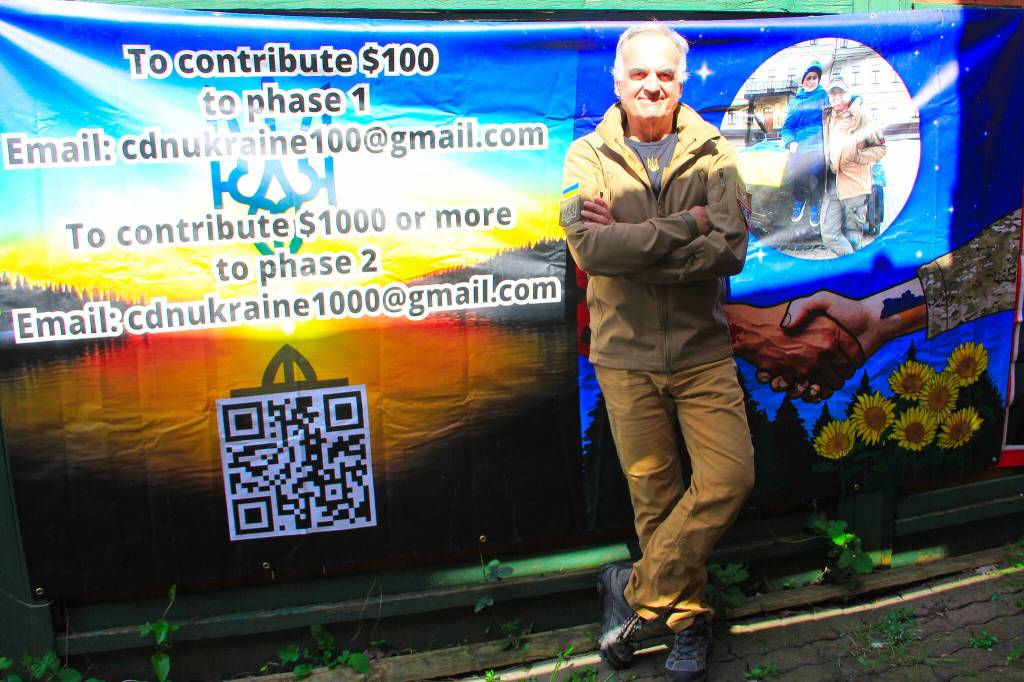 Cloverdale paramedic Will Rogers stands beside a banner he made up to advertise for a new investment fund he started to help both Ukraine and Canada. (Photo: Malin Jordan/Cloverdale Reporter)