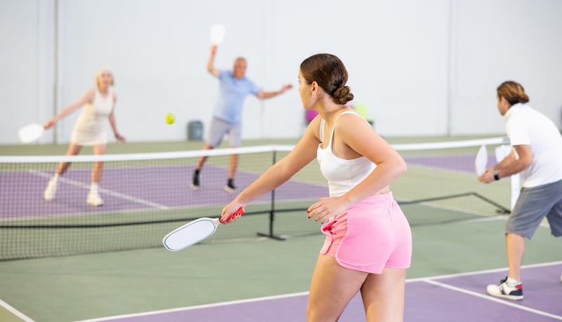 Rear view of young woman playing pickleball doubles on indoor court