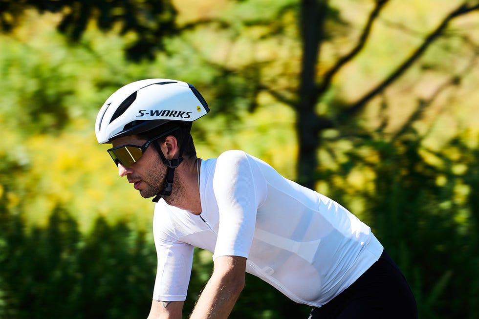 Cyclist wearing a white helmet and sunglasses riding through a sunny, leafy park. Cyclist wearing a white helmet and sunglasses riding through a sunny, leafy park.