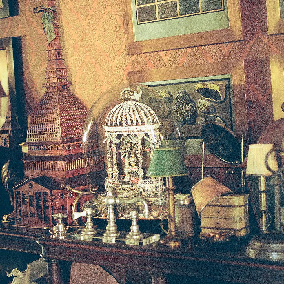 Antique wooden models and glass dome on cluttered desk with art on the wall in vintage setting.
