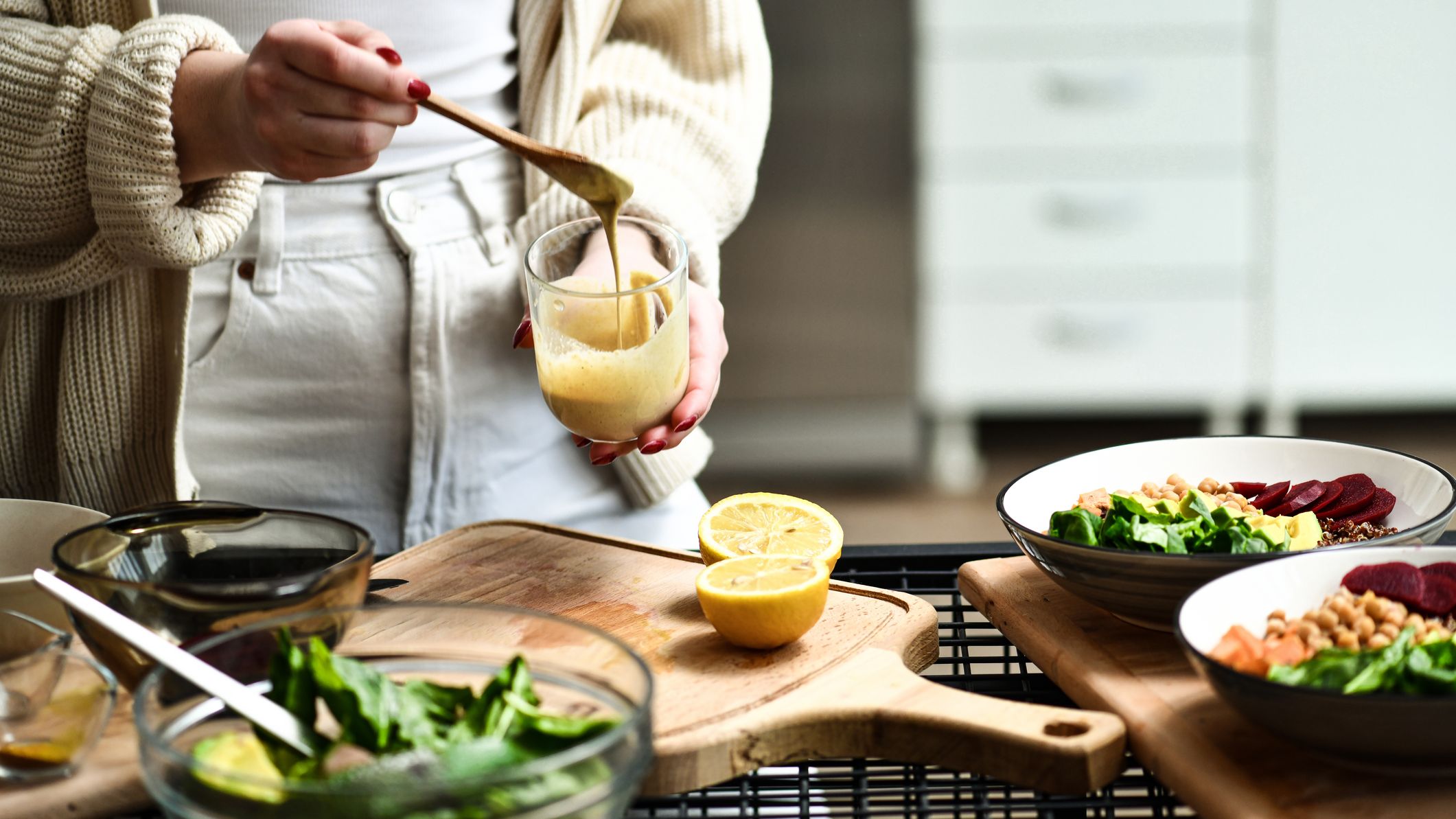 Woman stirring dressing, with chopping board in front of her with a halved lemon on it, and bowls with salad ingredients in them
