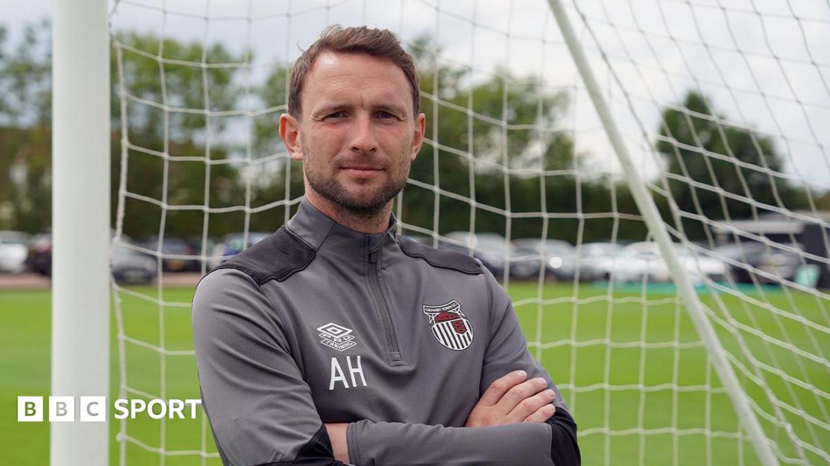 Alex Hughes posing for a picture while stood in a goal wearing a Grimsby Town tracksuit
