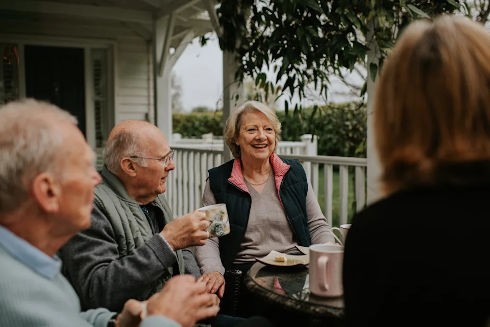 Four seniors enjoying a conversation and coffee on a porch, fostering a sense of community and well-being