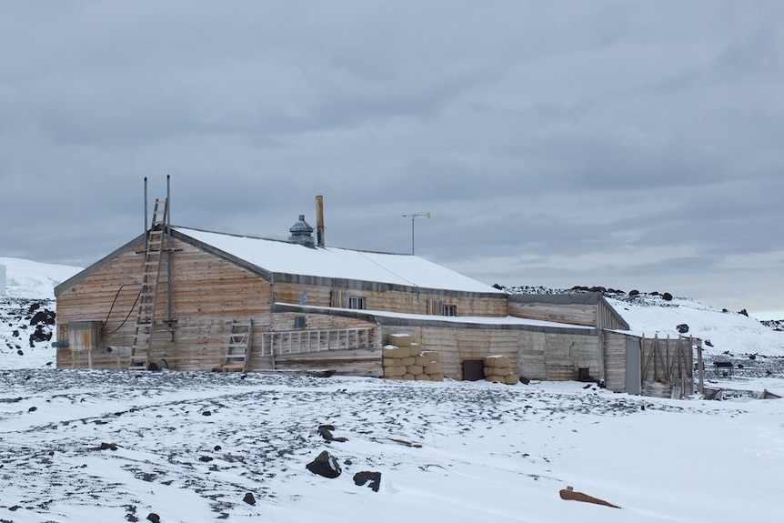 The long wooden structure, Scotts Terra Nova Hut, is situated in a snowy landscape, its roof dusted with snow.