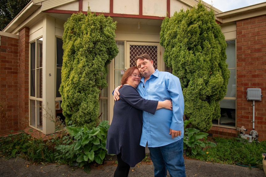 A couple in their fourties pose for a photo in front of their home