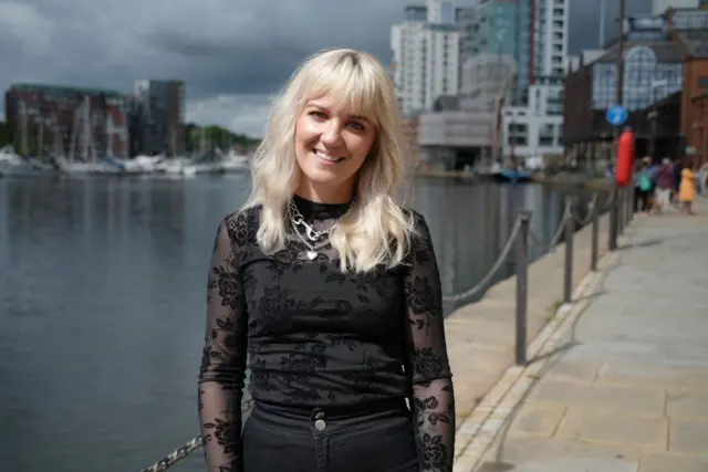 A woman with blonde hair and black clothes smiling at the camera