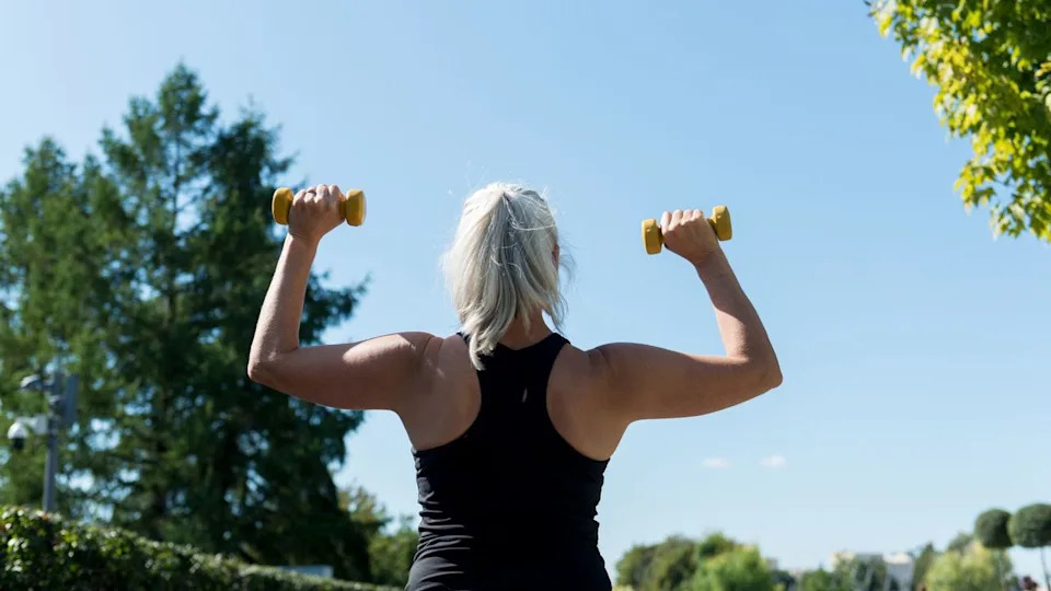 Woman with dumbbells in shoulder press overhead looking at the sky.