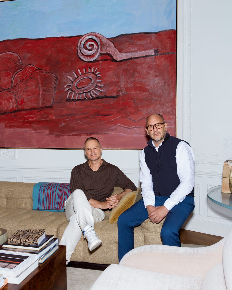 Two people sitting on a beige couch beneath a large abstract red and blue painting.