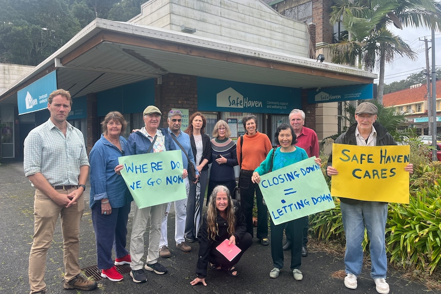 Eleven people gather outside Safe Haven Murwillumbah holding signs to protest the mental health service closure.