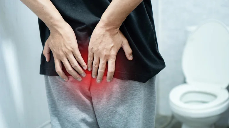 Man suffering from hemorrhoids or rectal pain holding his buttocks in bathroom. Concept of fissure, constipation, diarrhea, or colon cancer symptoms. Professional medical healthcare stock