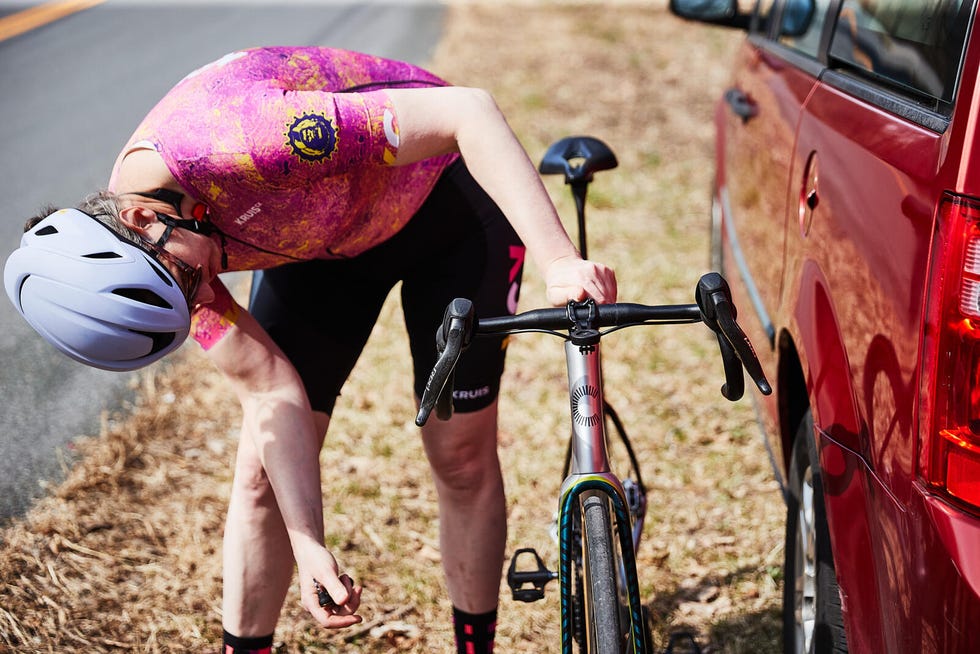 Cyclist adjusting bike near a red car on a roadside. Cyclist adjusting bike near a red car on a roadside.