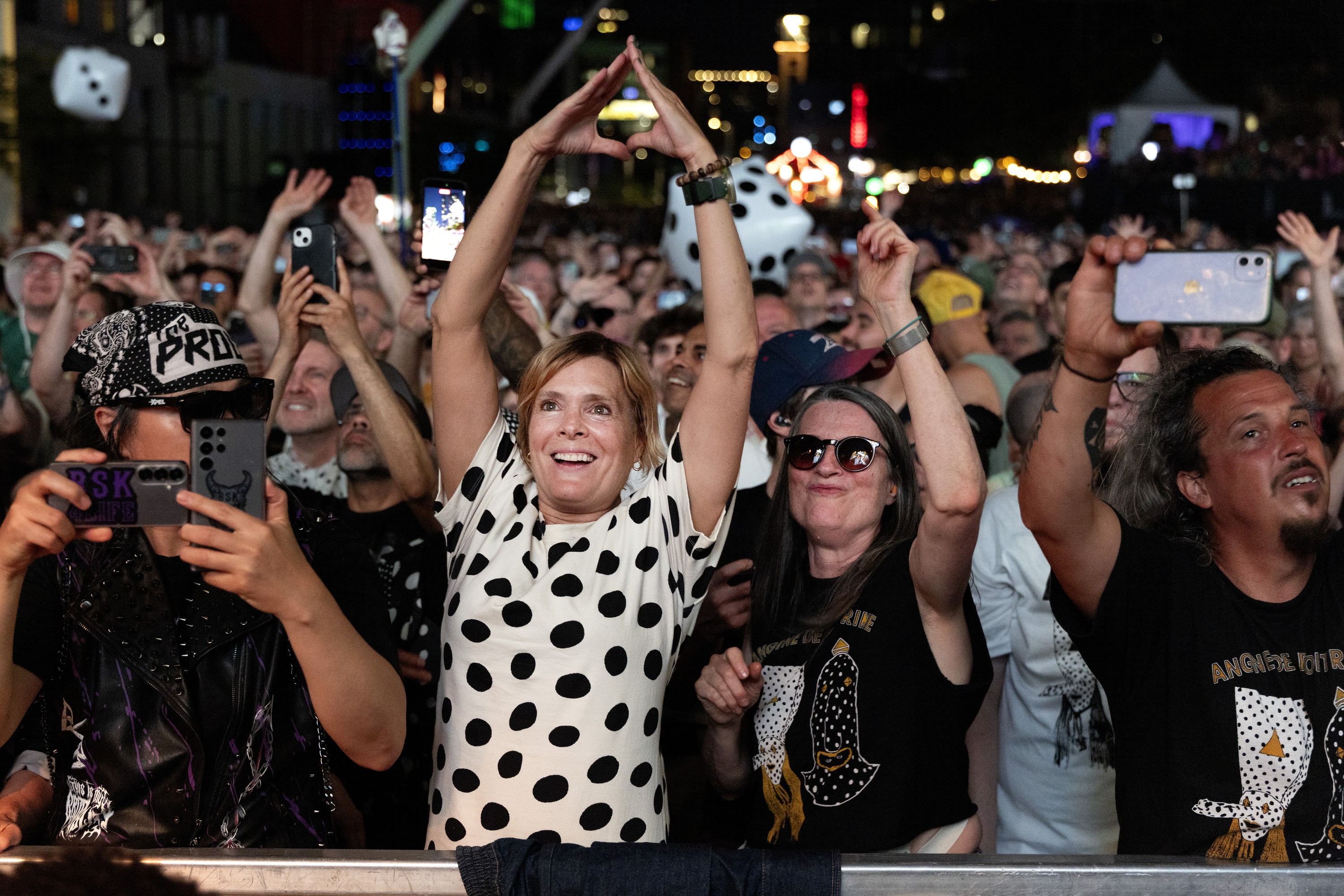 A fan makes a triangle hand gesture at the front of a large outdoor crowd at an Angine de Poitrine concert.