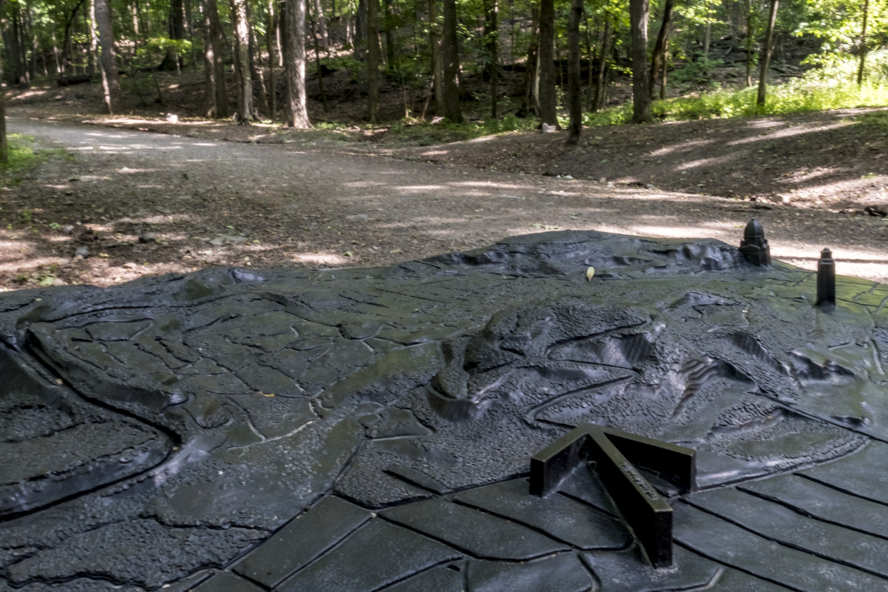 A metal relief map beside a gravel path in a park.