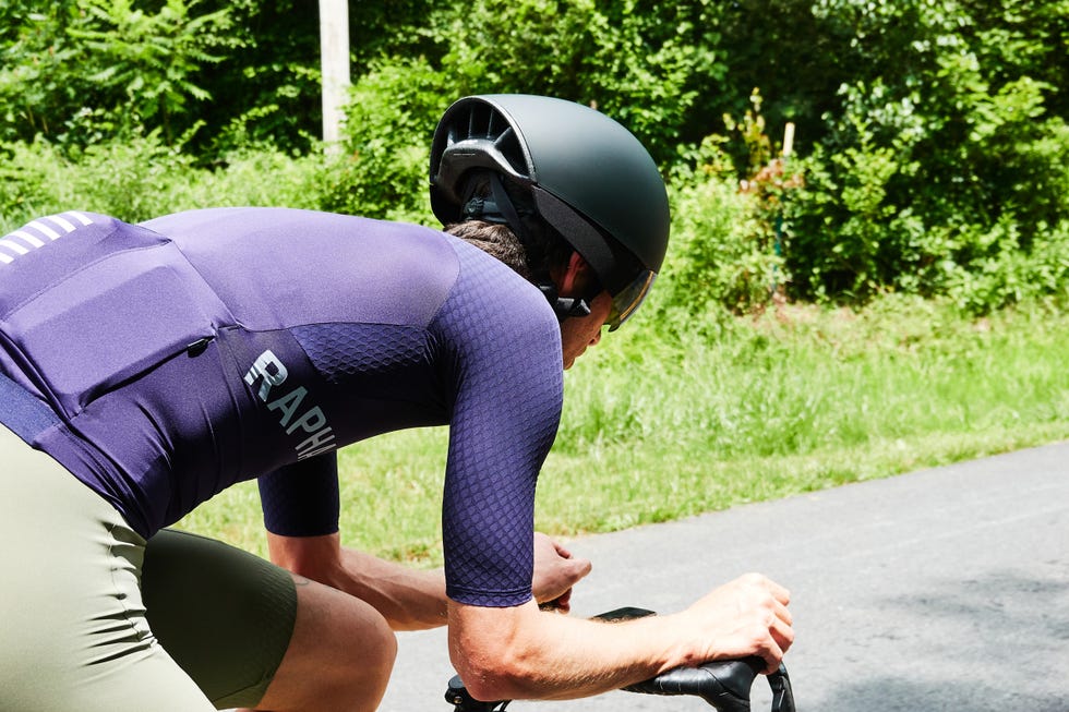 Cyclist in blue gear riding on a sunny road with greenery in the background. Cyclist in blue gear riding on a sunny road with greenery in the background.
