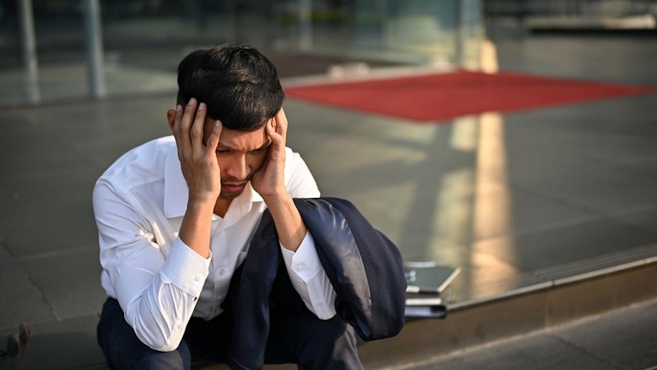 Man in suit, sitting on street curb looking stressed