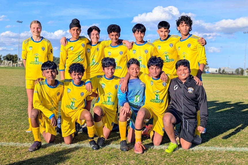 Thirteen soccer players posing for a photo at a soccer ground