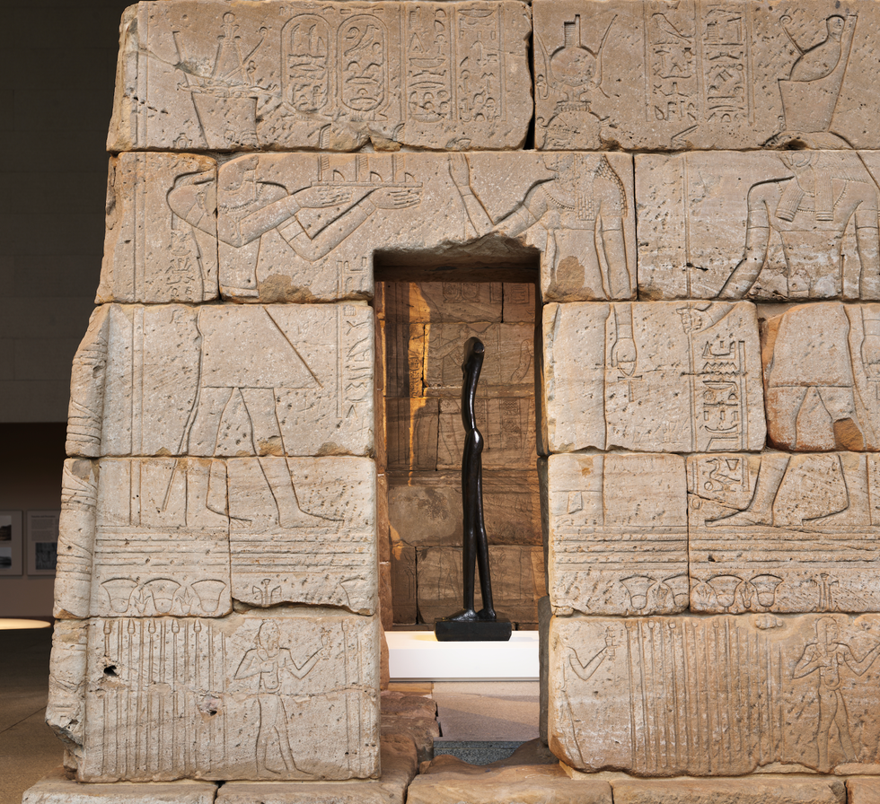 Ancient stone wall with hieroglyphs and a black sculpture in doorway.