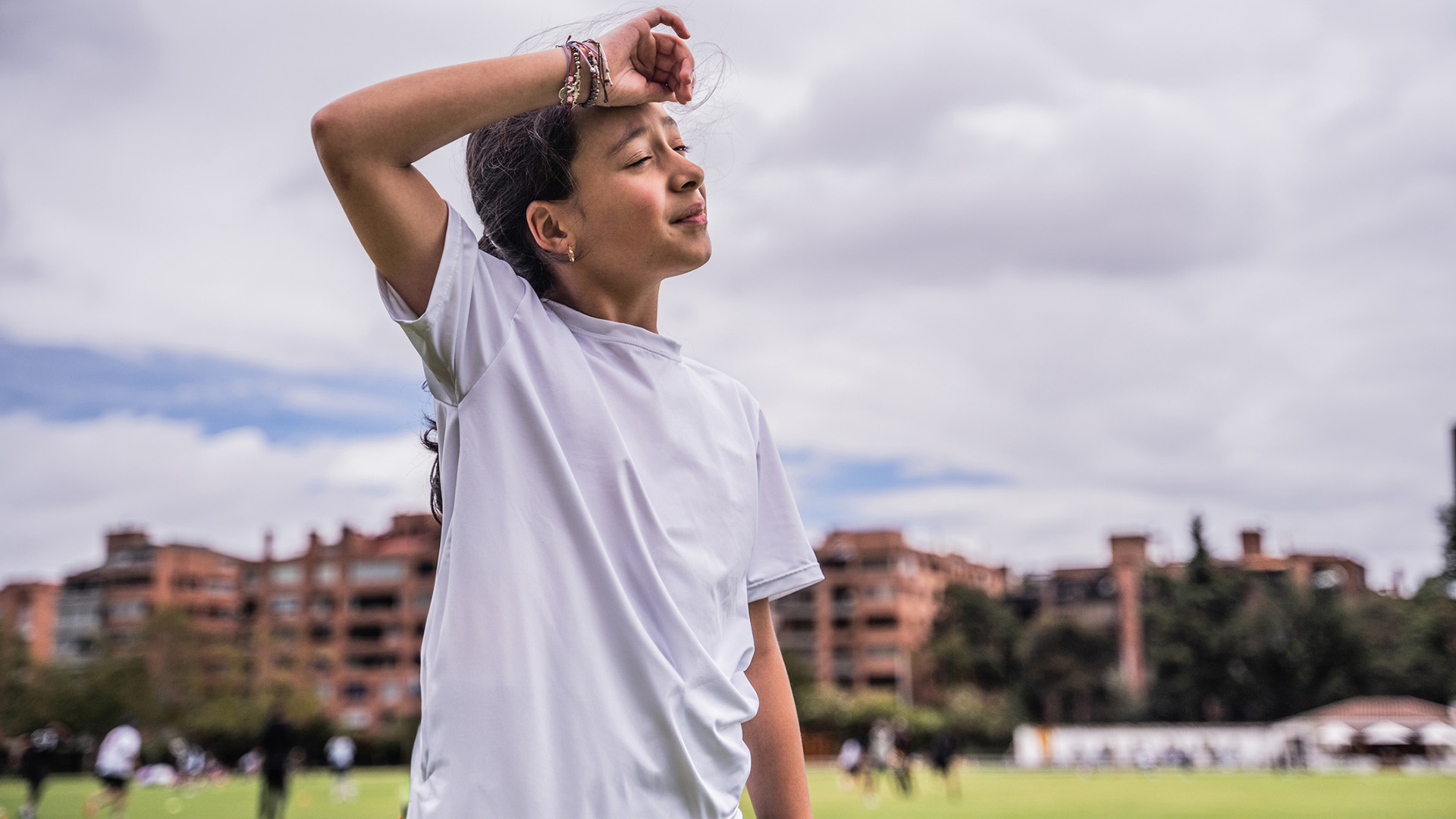 A young girl wearing a white t-shirt puts a hand to her head.