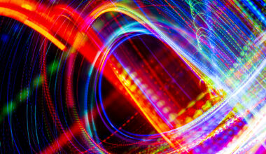 Abstract long-exposure light trails in swirling patterns of red, blue, green, and white against a black background.