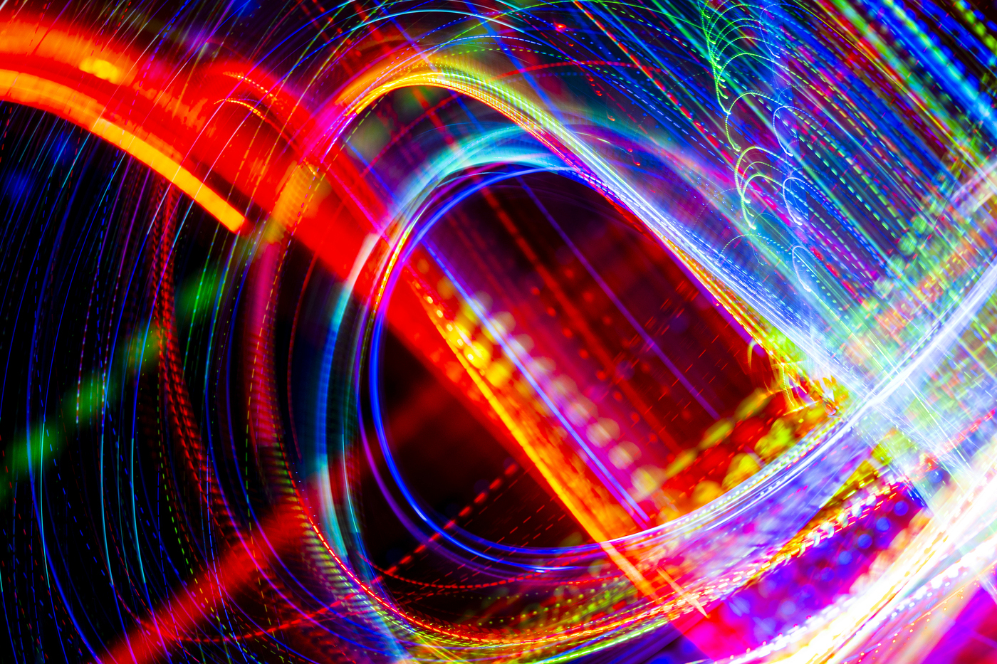 Abstract long-exposure light trails in swirling patterns of red, blue, green, and white against a black background.