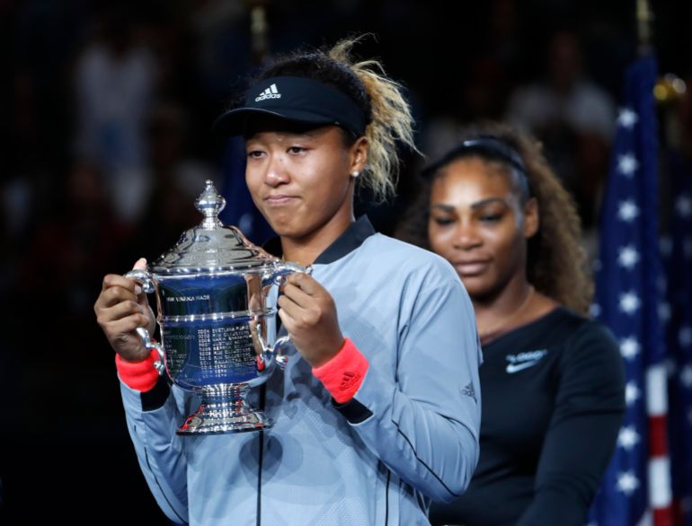 FILE - Naomi Osaka, of Japan, holds the trophy after defeating Serena Williams, rear, in the women's final of the U.S. Open tennis tournament in New York, in this Saturday, Sept. 8, 2018, file photo. Naomi Osaka withdrew from the French Open on Monday, May 31, 2021, and wrote on Twitter that she would be taking a break from competition, a dramatic turn of events for a four-time Grand Slam champion who said she experiences “huge waves of anxiety” before speaking to the media and revealed she has “suffered long bouts of depression.” (AP Photo/Adam Hunger, File)
