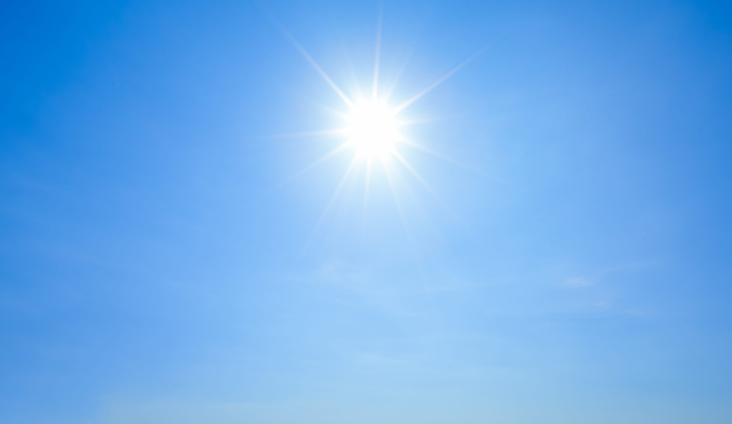 Shining sun with rays and clear blue sky background.