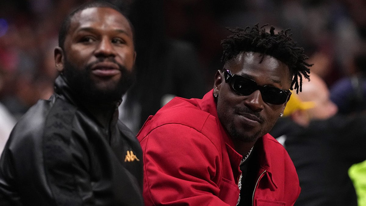 Floyd Mayweather Jr. sitting with Antonio Brown during a basketball game.