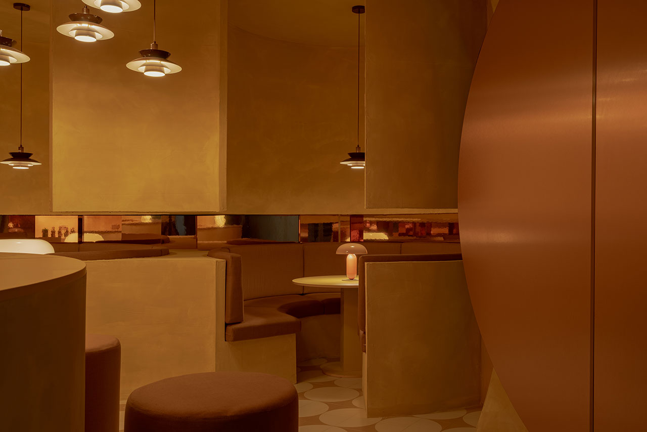 A modern cafe interior with warm amber lighting, circular pendant lamps, brown cushioned seating, and round tables in a minimalist design.
