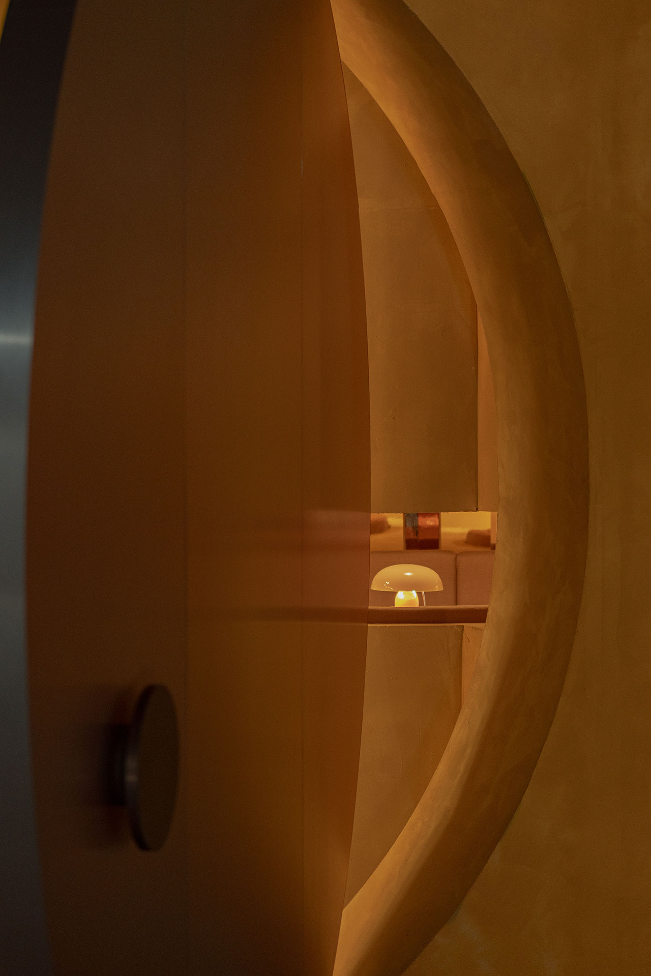 A round doorway with warm brown walls frames a small table and lamp in the background. The scene is softly lit, creating a cozy atmosphere.