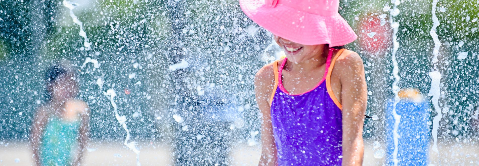 Child wearing hat and playing in an outdoor spray pad