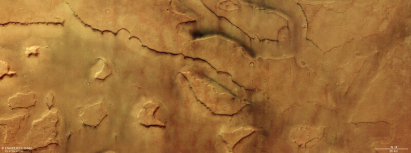 Looking down at an orangish-brown landscape with ridges, small craters and tiny white nubs.