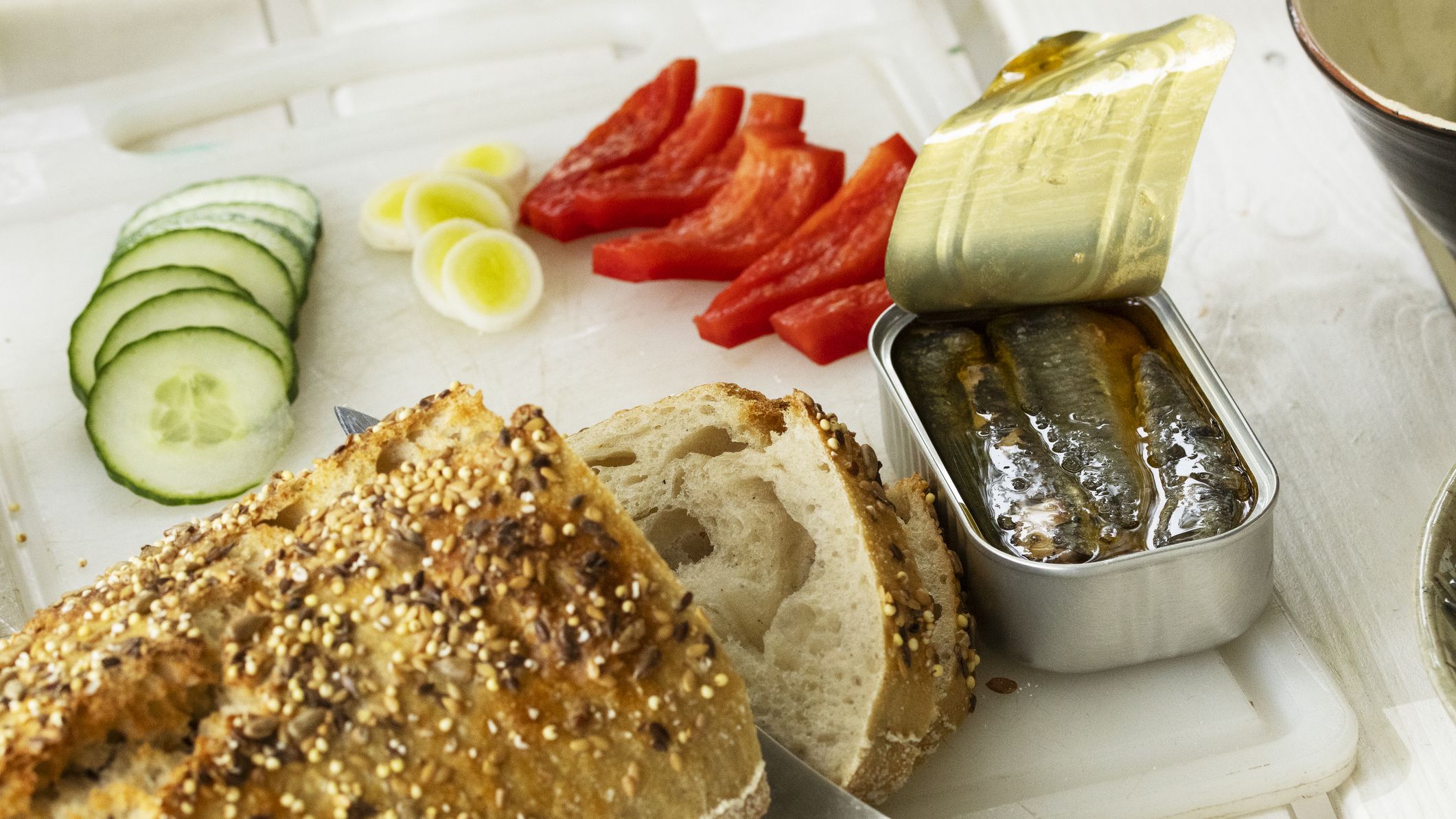Spread of bread, sliced cucumbers, leeks and red pepper, and an open tin of sardines