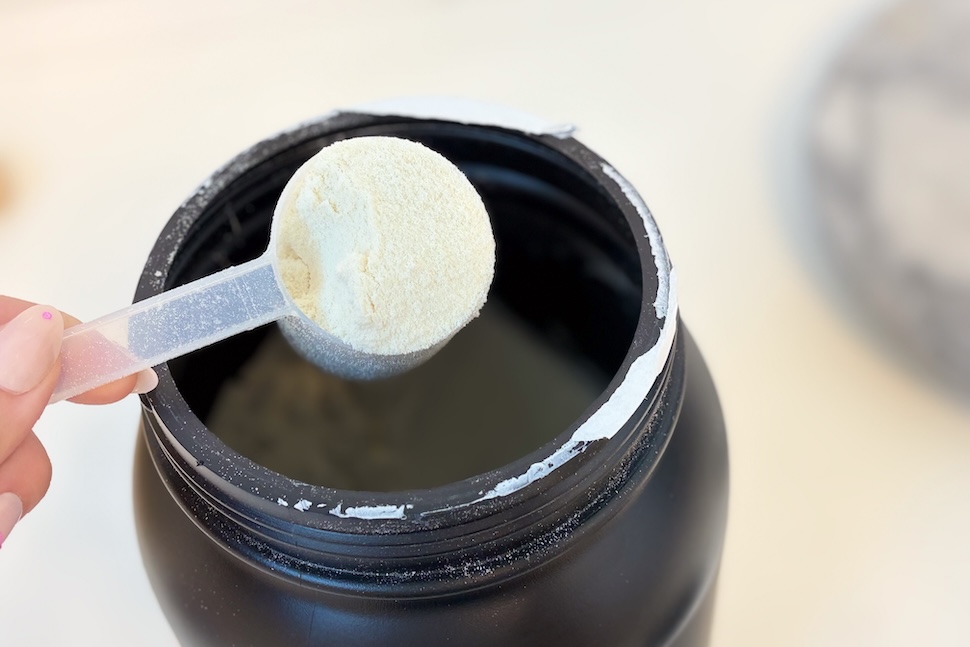 Closeup shot of a hand holding a plastic scoop, packed to the brim with the off-white powder of Factor Form Meal Replacement.