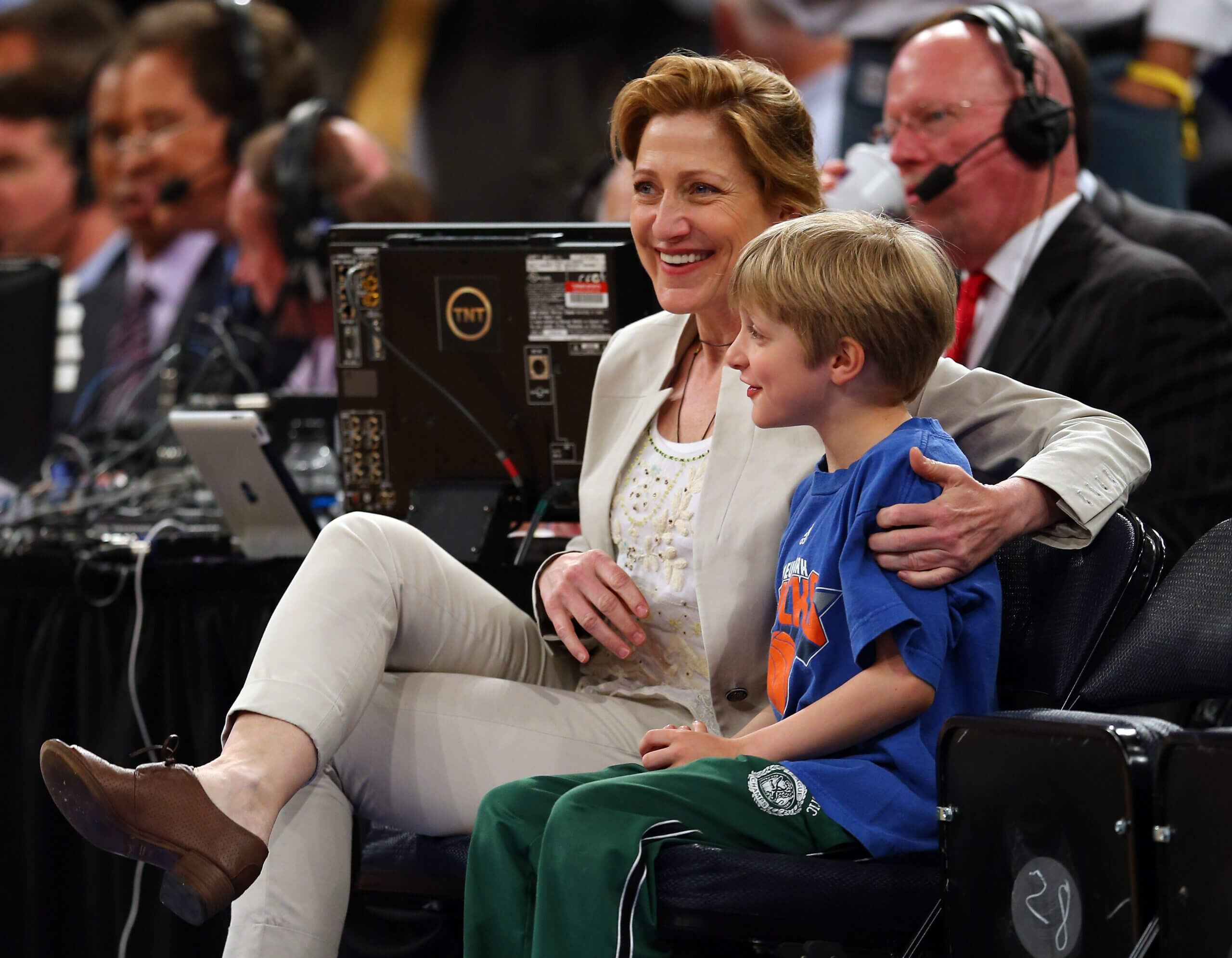 Edie Falco sits courtside with her son, her arm around his shoulder, in 2013.